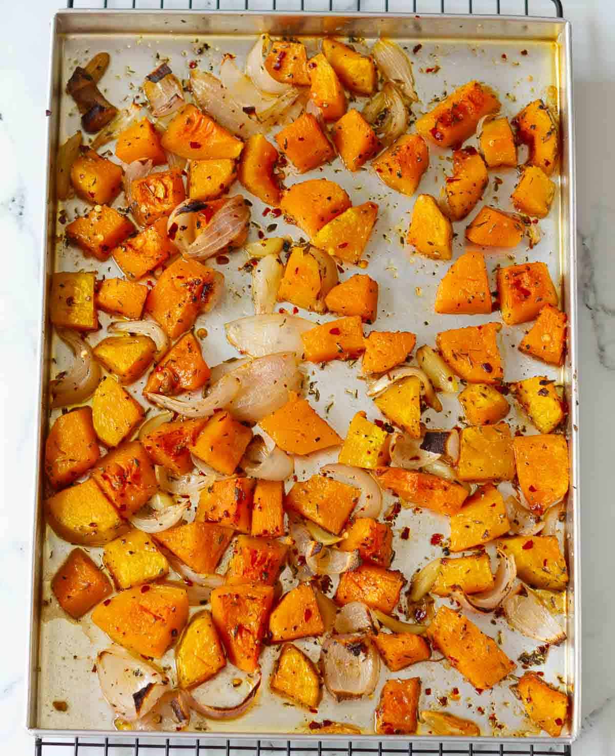 Roasted pumpkin, onion, and garlic on a baking tray.