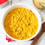Pumpkin macaroni cheese in a white pot with a wooden spoon on the side.