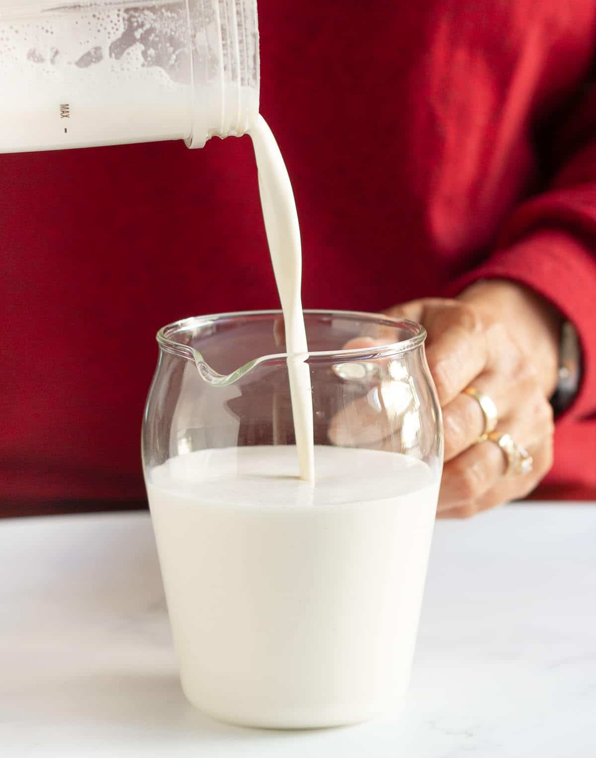 Cashew milk being poured from a blender jar into a glass pitcher.