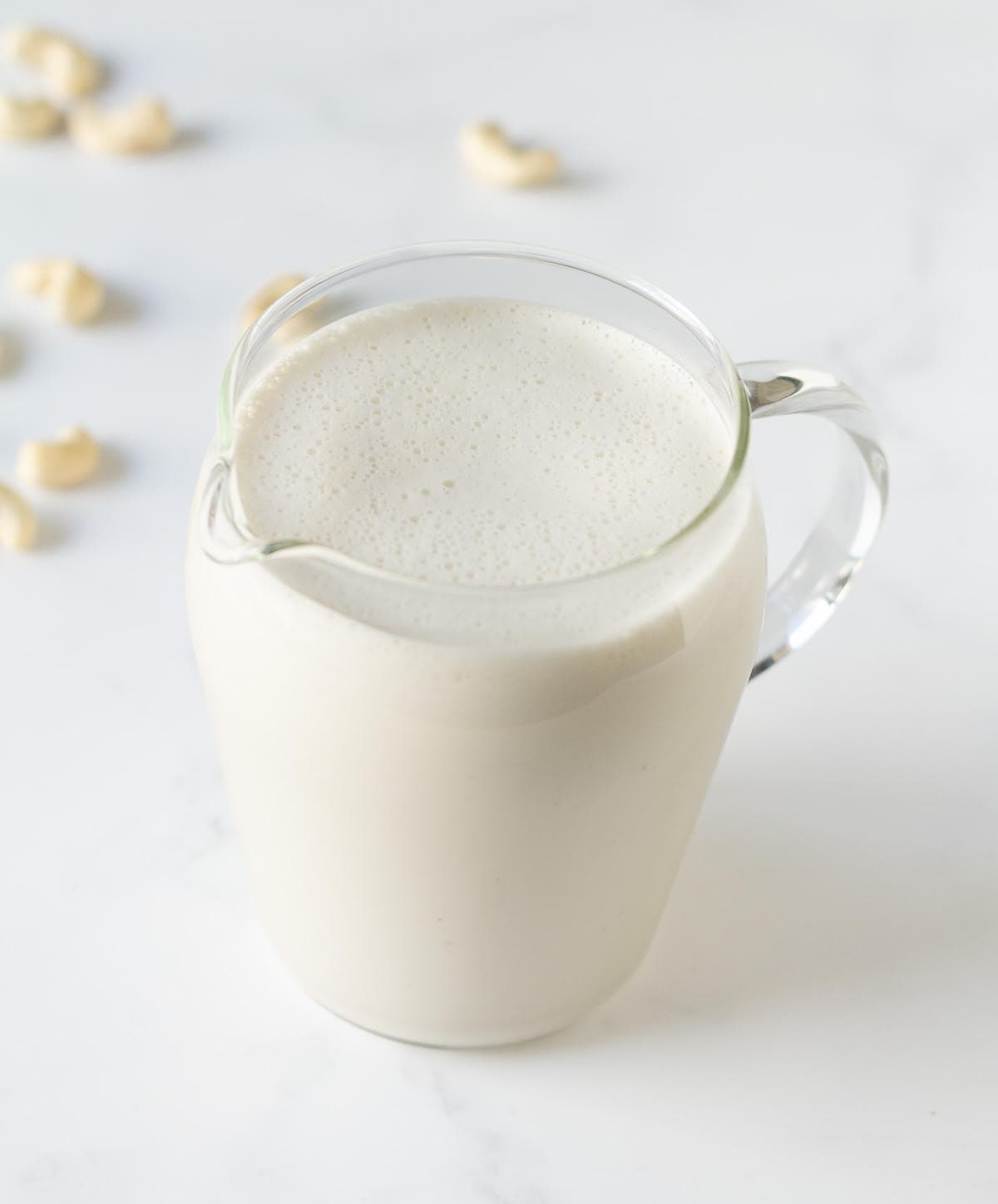 cashew milk in a pitcher with some cashews in the background.