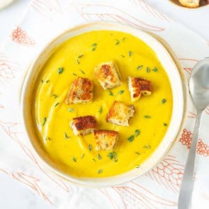 roasted sweet potato soup in a bowl garnished with croutons and thyme.
