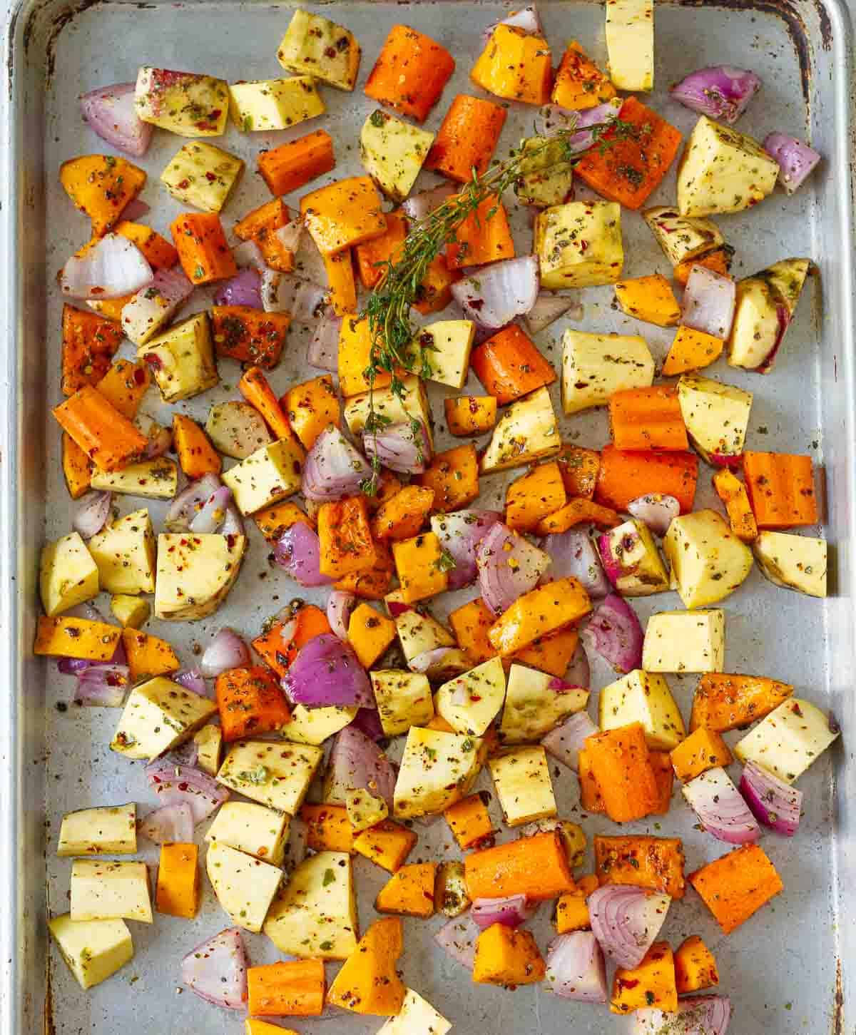 chopped vegetables tossed in olive oil and spices on a baking tray.