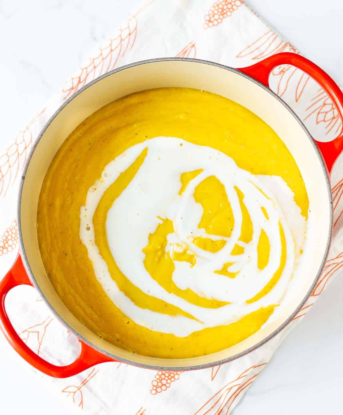 coconut milk poured on top of sweet potato soup in a saucepan.