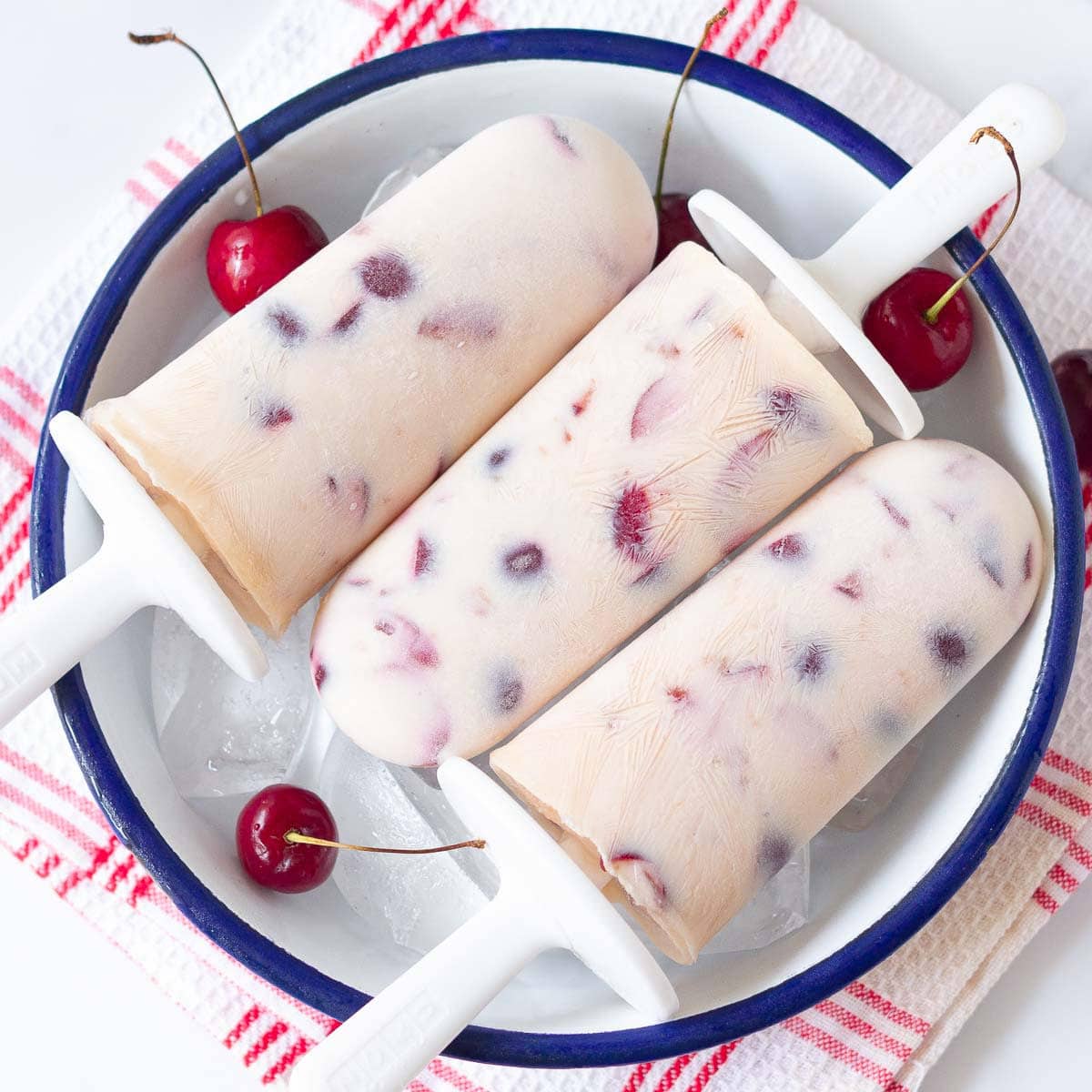 3 cherry popsicles in a bowl with ice and fresh cherries.