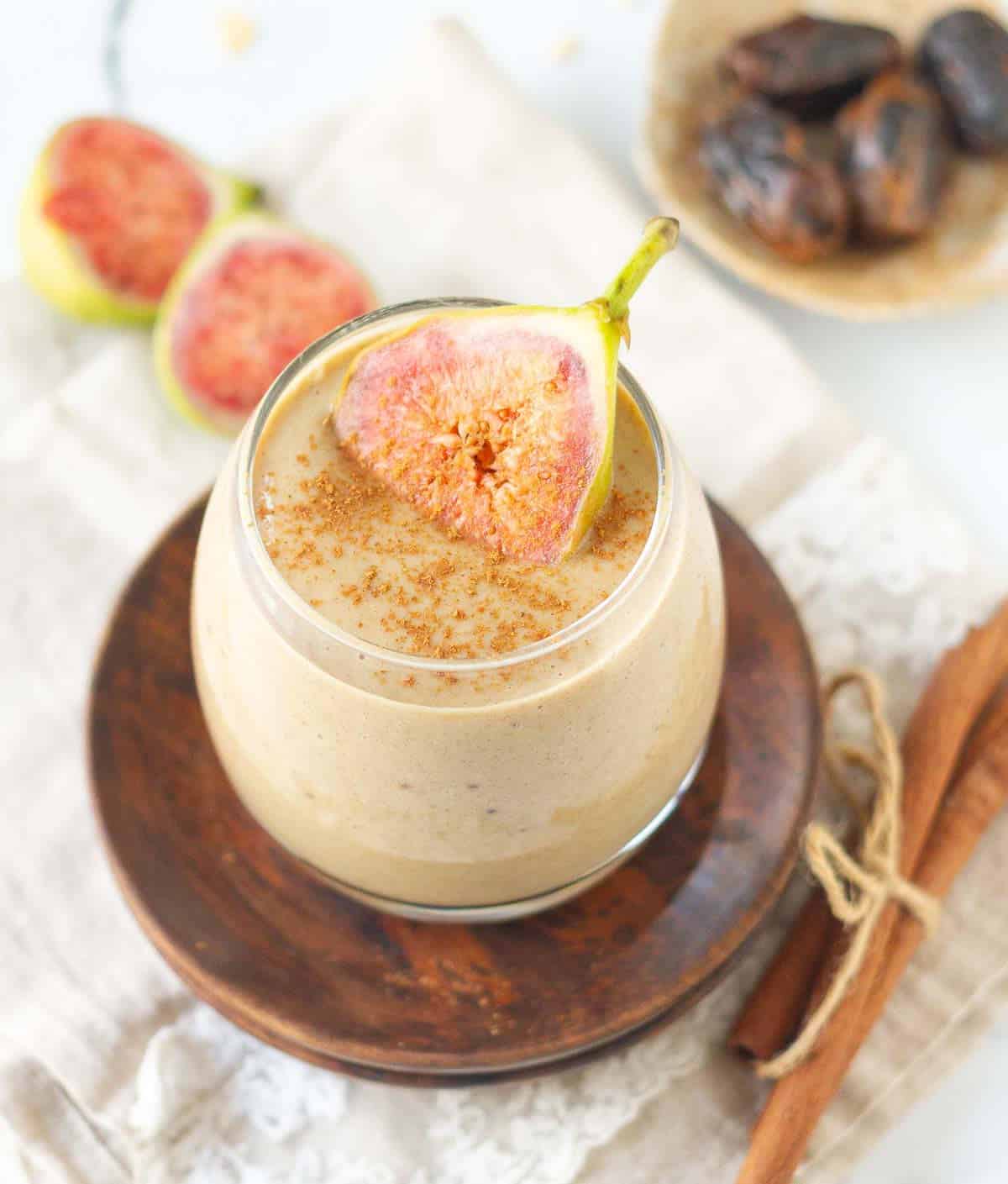 fig smoothie in a glass on a wooden plate topped with a slice of fresh fig.