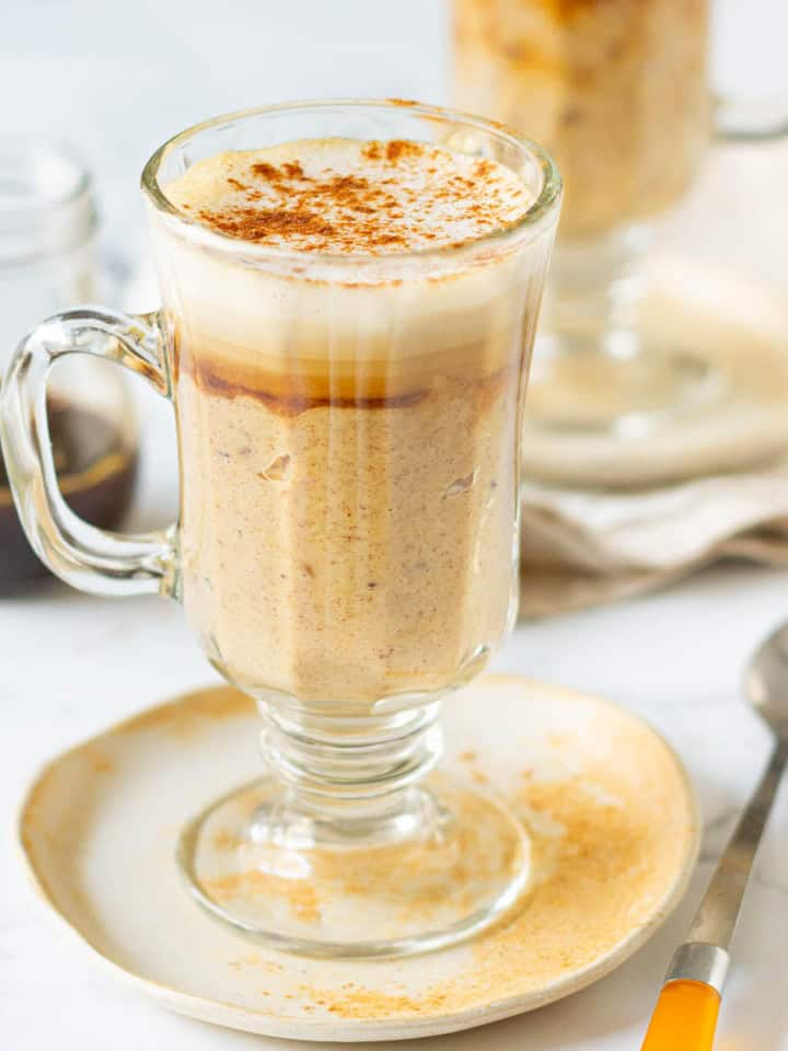 oatmeal latte in a clear glass mug on a small plate with a spoon.