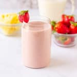 Pineapple strawberry smoothie in a glass with a strawberry on the rim.