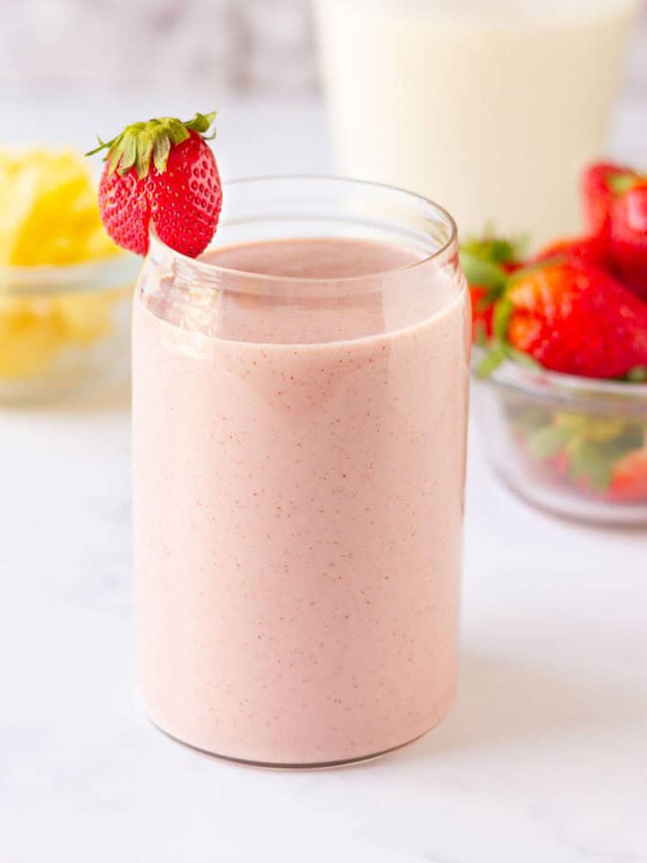 Pineapple strawberry smoothie in a glass with a strawberry on the rim.