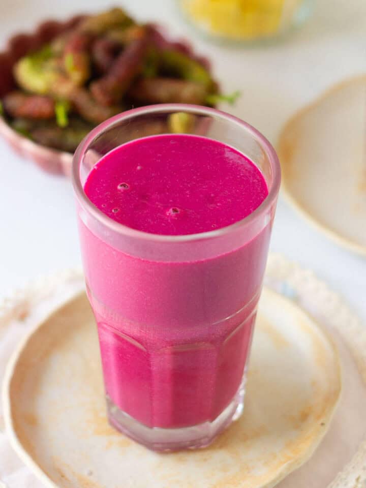 Mulberry mango smoothie in a glass on a small plate.