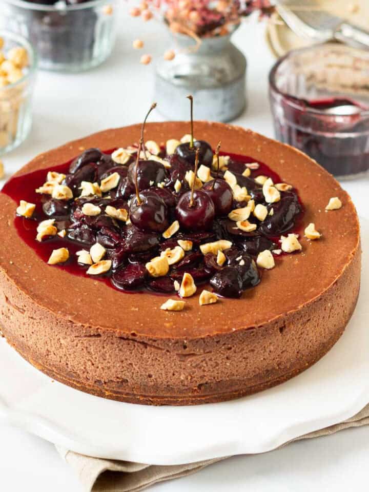 Chocolate hazelnut cheesecake with cherry sauce and hazelnuts on top on a platter.