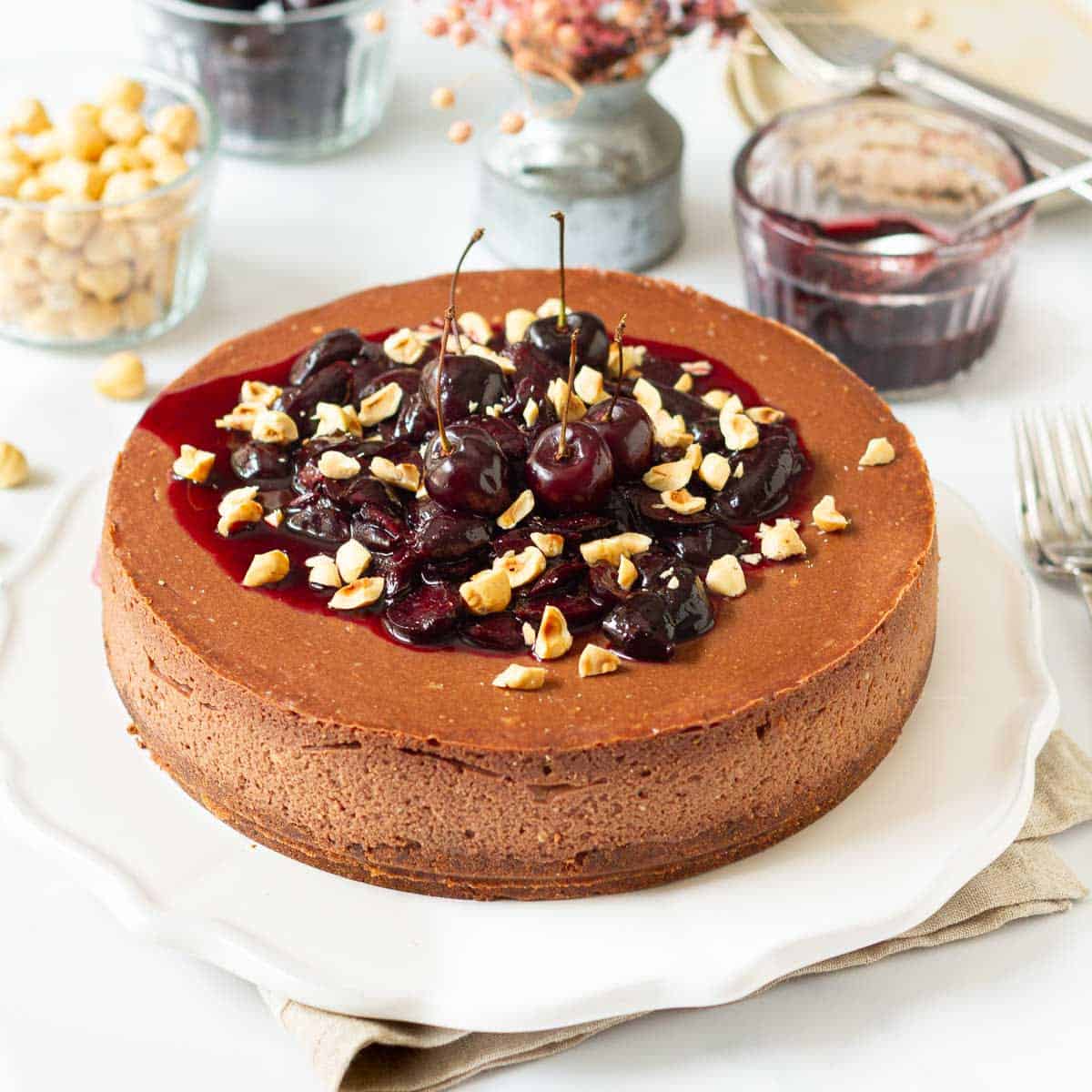 Chocolate hazelnut cheesecake with cherry sauce and hazelnuts on top on a platter.