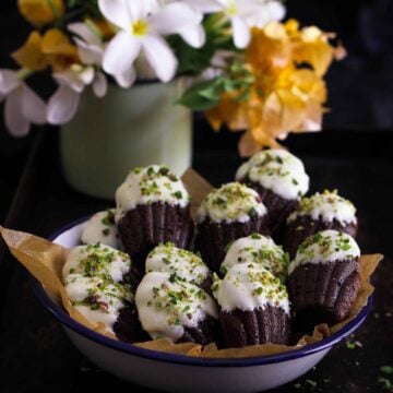 chocolate madeleines in a paper-lined bowl with flowers in the background.