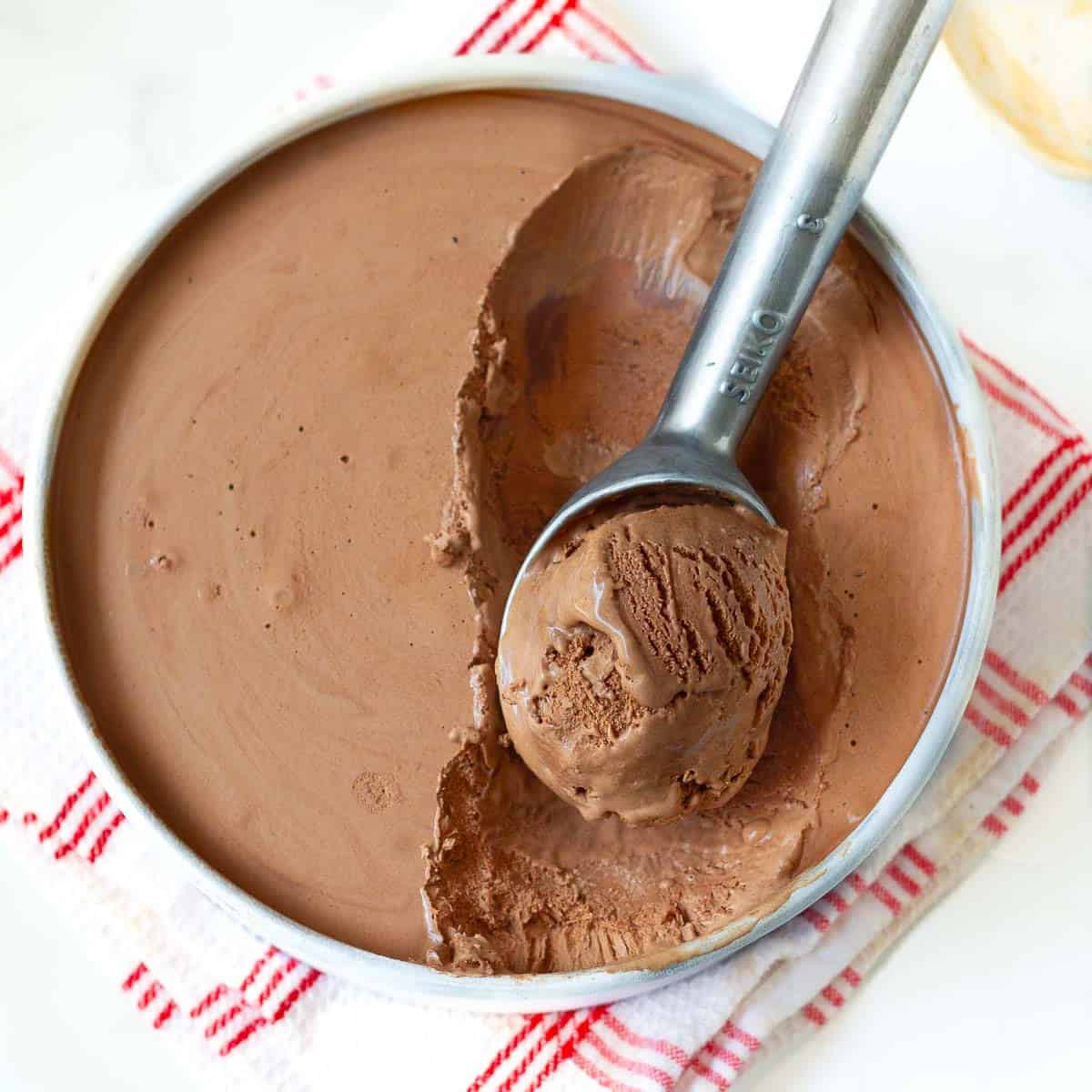 Ice cream in a pan with a scoop taken out with an ice cream scooper.