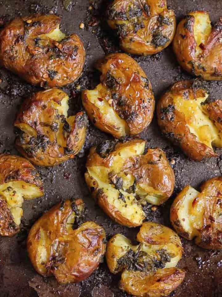 Crispy smashed potatoes with garlic and basil on a black tray.