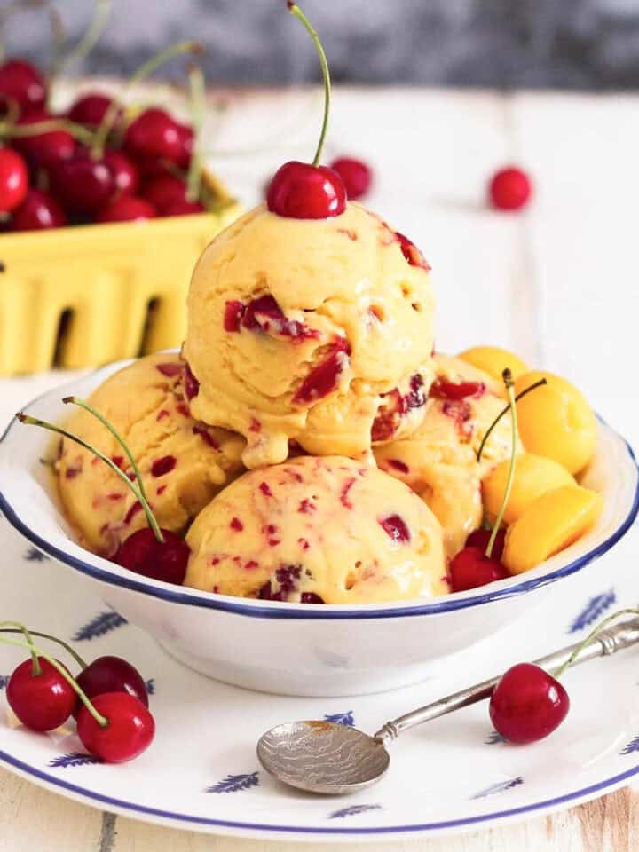 Scoops of mango cherry frozen yogurt in a bowl with a cherry on top.