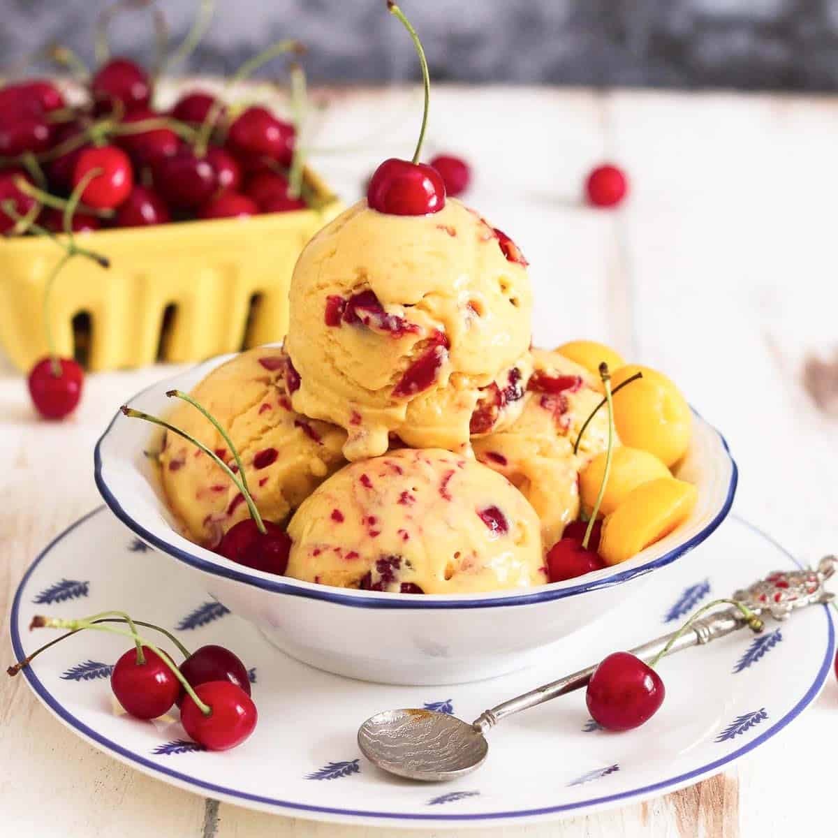 Scoops of mango cherry frozen yogurt in a bowl with a cherry on top.