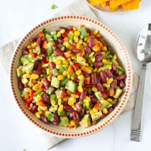 A bowl of corn bean and veggie salad with a spoon on the side.