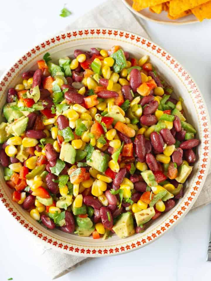 A bowl of corn bean and veggie salad with a spoon on the side.