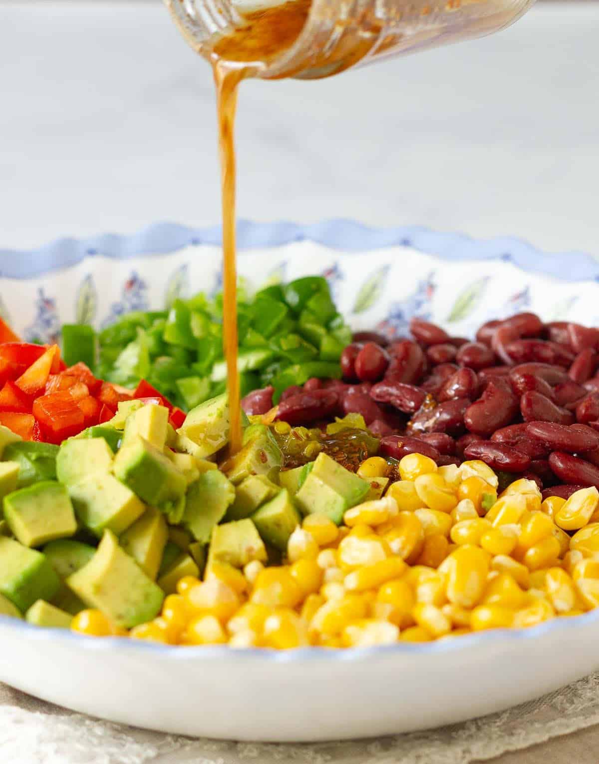 Dressing being poured from a jar on to a bowl of salad.