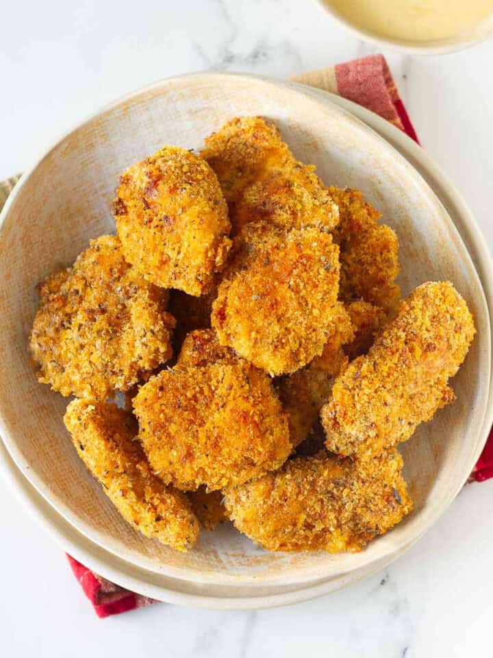 A bowl of chicken nuggets with sauce on the side.