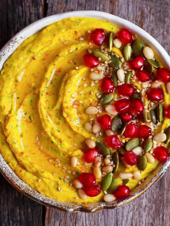 Hummus in a bowl with pomegranate arils, nuts and pumpkin seeds.