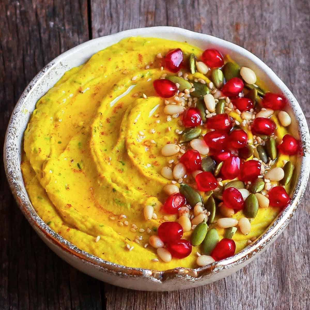 Carrot hummus in a bowl with olive oil, pomegranate, nuts and pumpkin seeds.