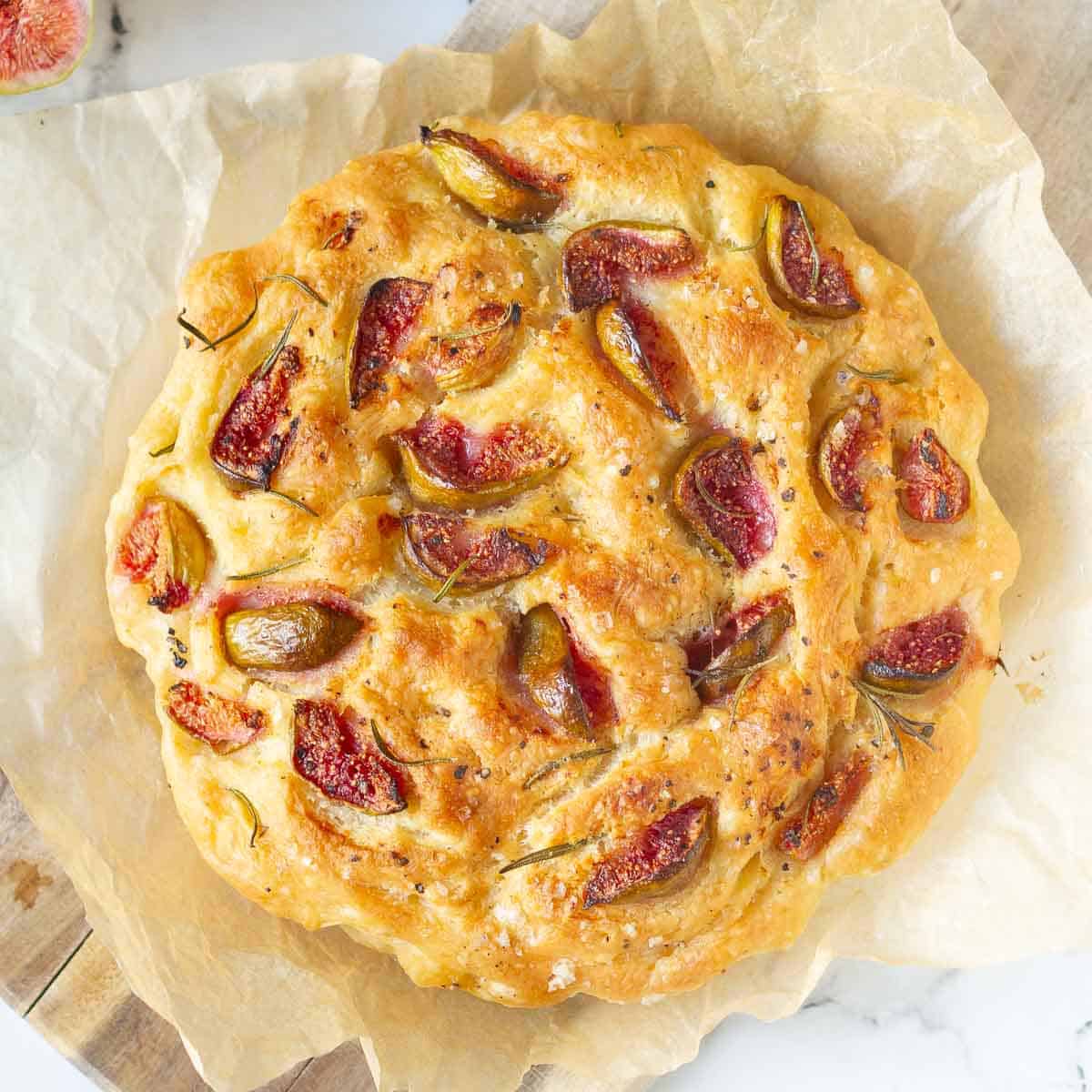 A loaf of focaccia with figs and rosemary on parchment paper.