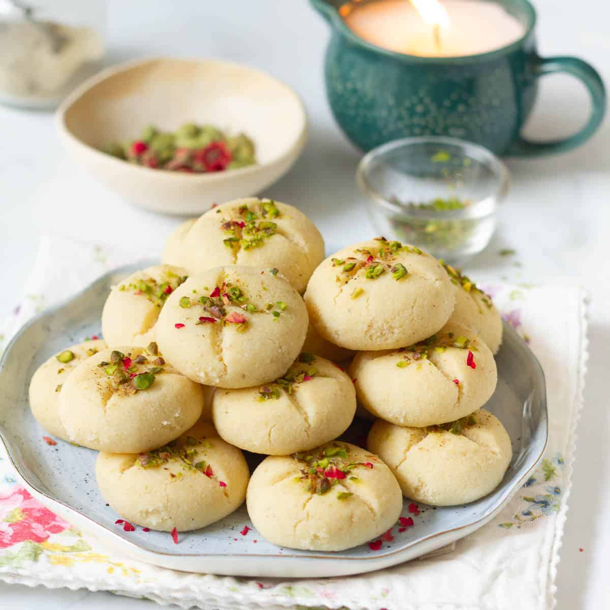 A stack of cookies topped with pistachios , cardamom powder, and dried rose petals.