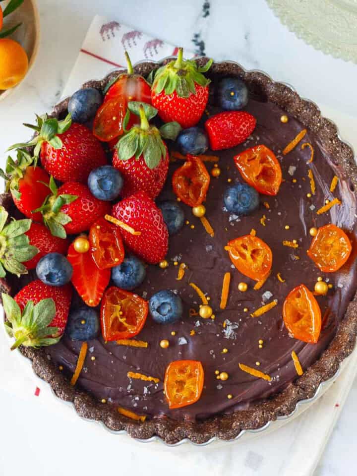 chocolate orange tart garnished with berries, orange zest, candied oranges on a white napkin.