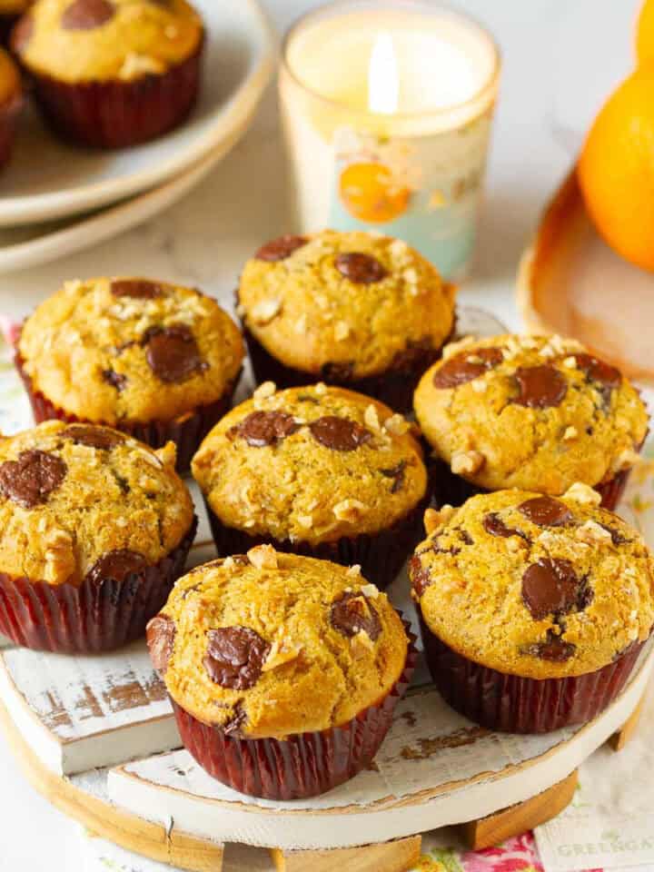 Muffins topped with chocolate chips on a white tray with a candle and oranges around.