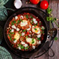 A cast iron pan with tomato sauce and cooked eggs with ingredients around.