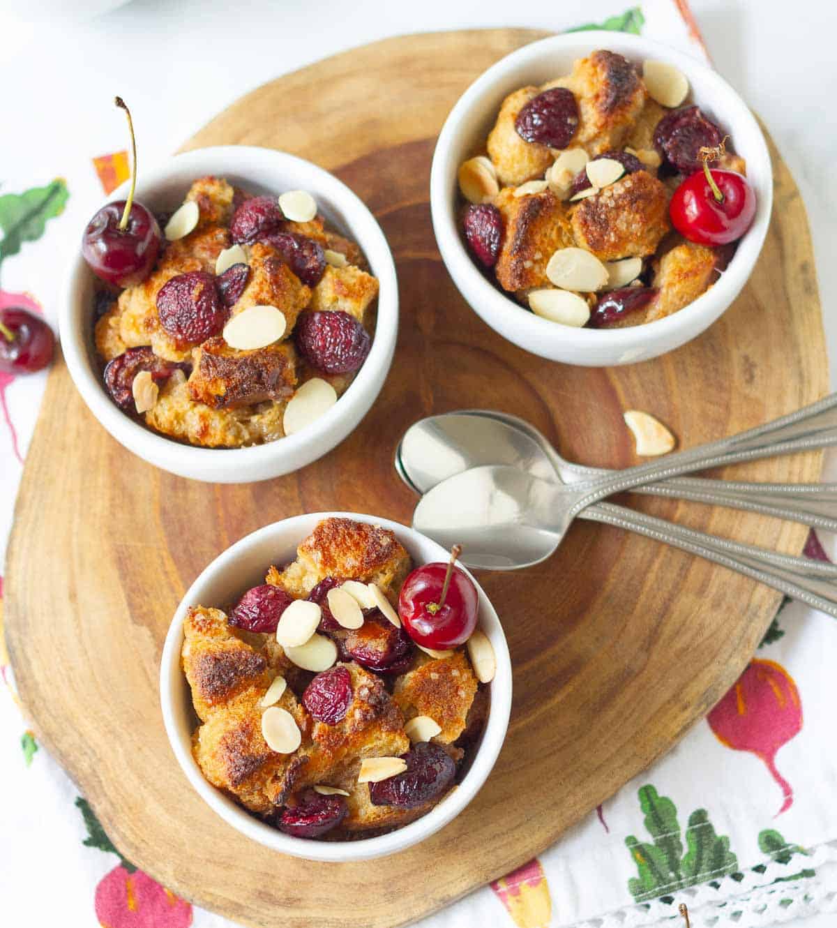 3 white ramekins with cherry bread pudding with 3 spoons.