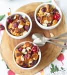 3 ramekins with cherry bread pudding on a wooden board.