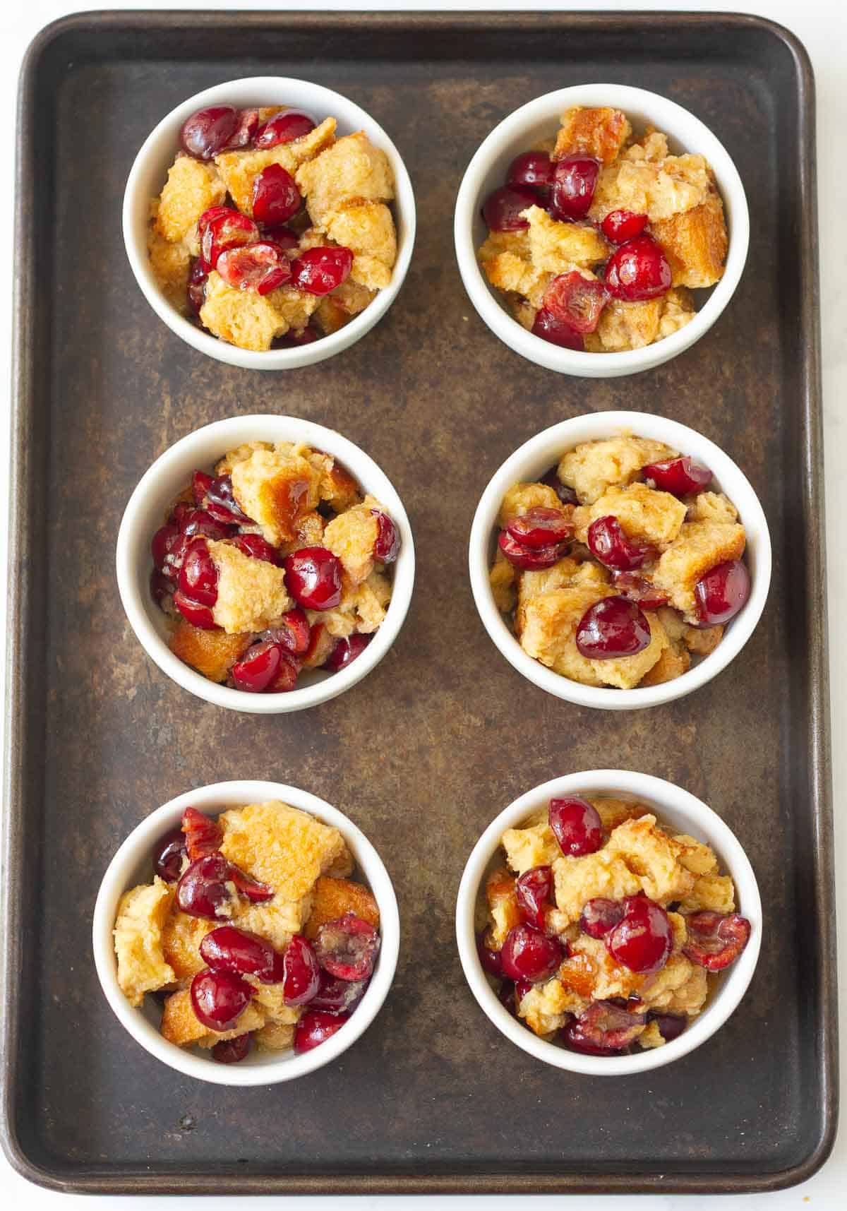 Bread pudding mixture in 6 ramekins on a black tray.
