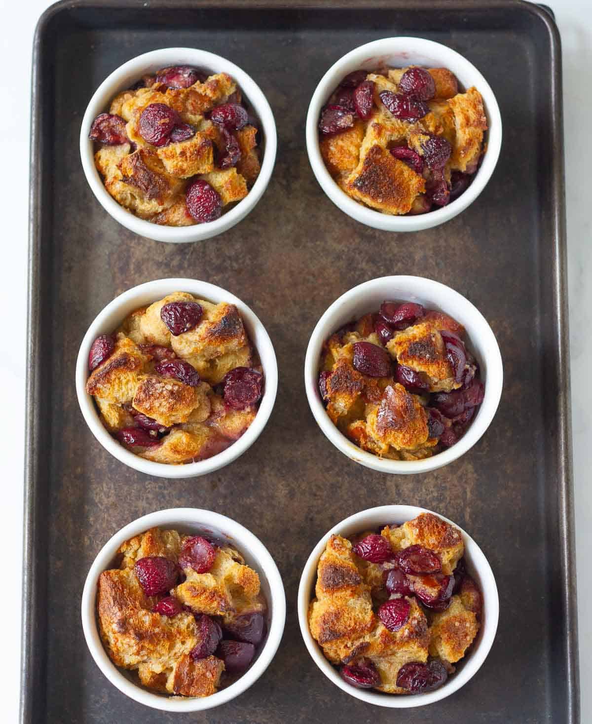 Baked bread pudding in 6 ramekins on a black tray.