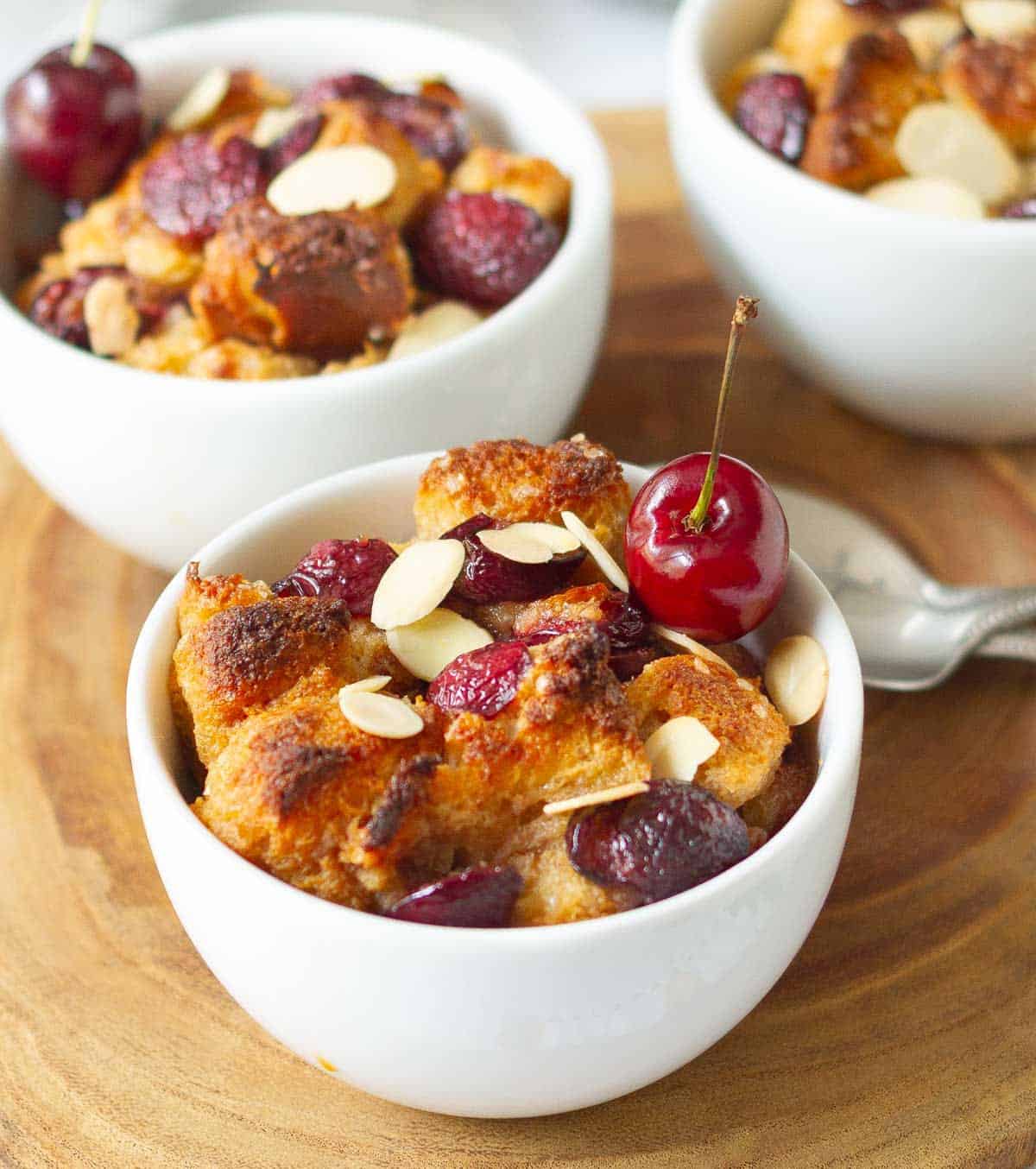 Cherry bread pudding with almonds and fresh cherry in a white ramekin.
