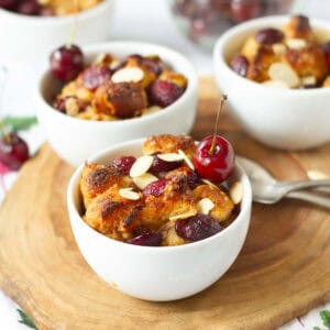 cherry bread pudding in 3 ramekins with spoons on the side on a wooden board.