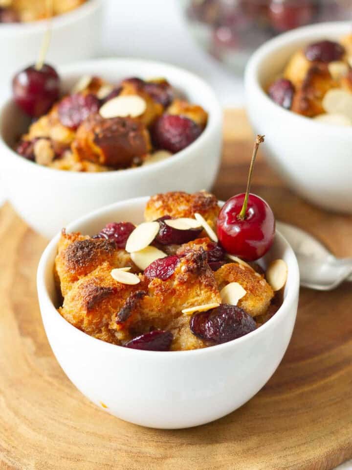 cherry bread pudding in 3 ramekins with spoons on the side on a wooden board.