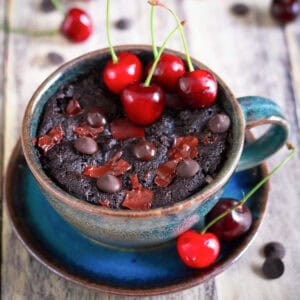 Chocolate cherry mug cake in a blue cup, topped with fresh cherries and chocolate.