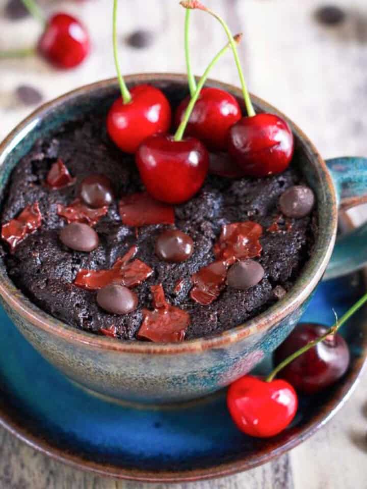 Chocolate cherry mug cake in a blue cup, topped with fresh cherries and chocolate.