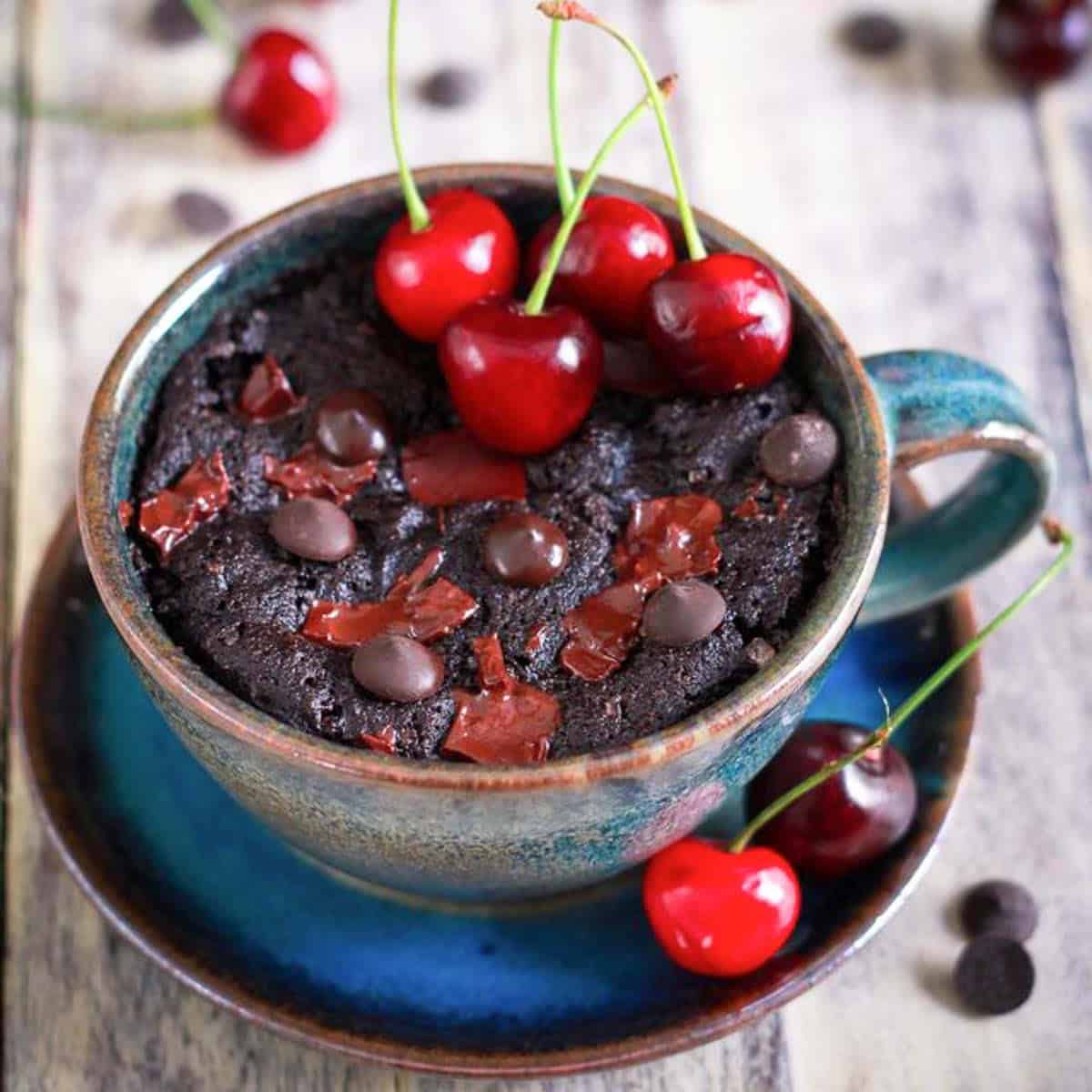 Chocolate cherry mug cake in a blue cup, topped with fresh cherries and chocolate.