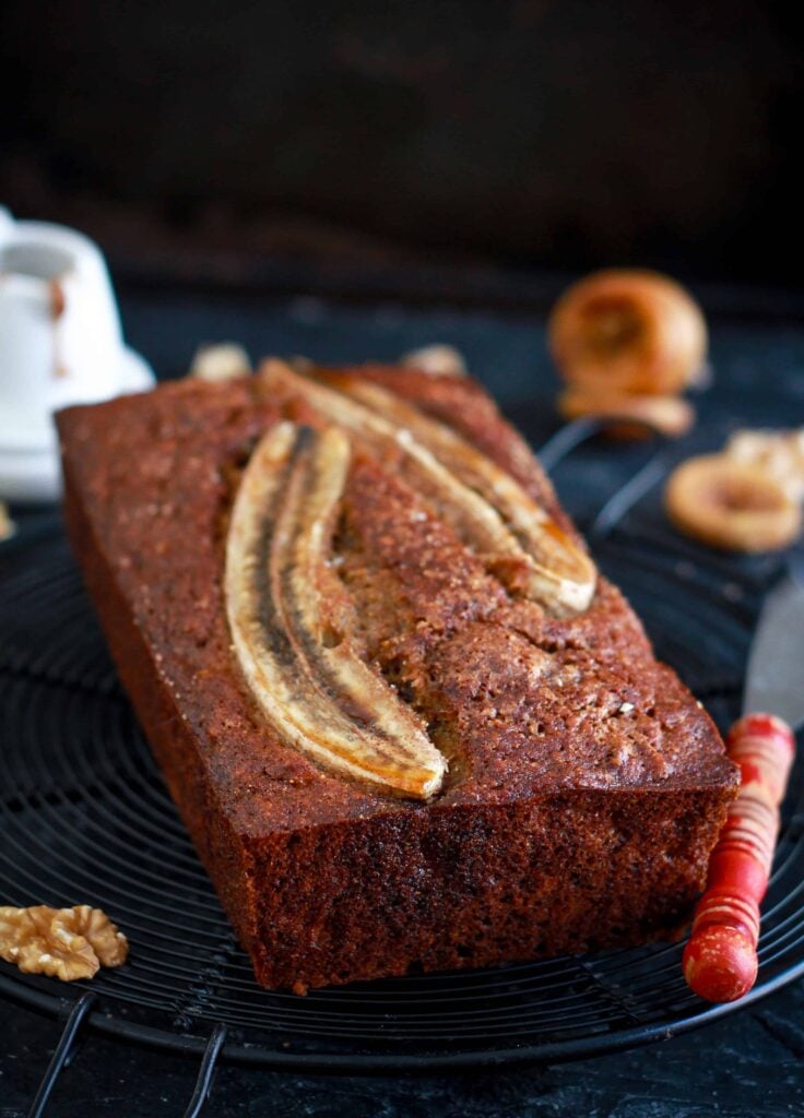 loaf of walnut banana bread with a knife on a trivet.