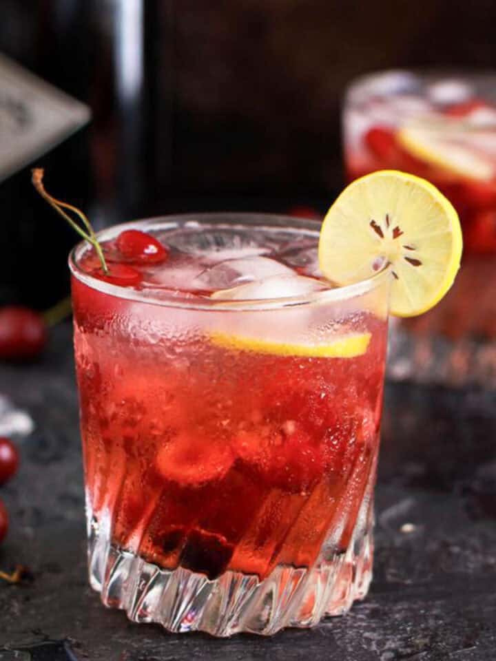 Cherry gin and tonic in a glass with a slice on lemon.