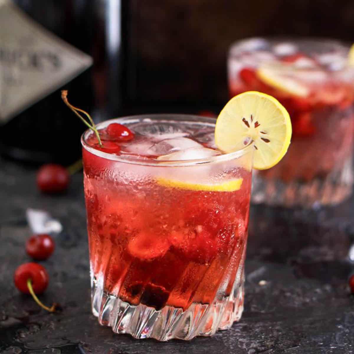 Cherry gin and tonic in a glass with a slice on lemon.