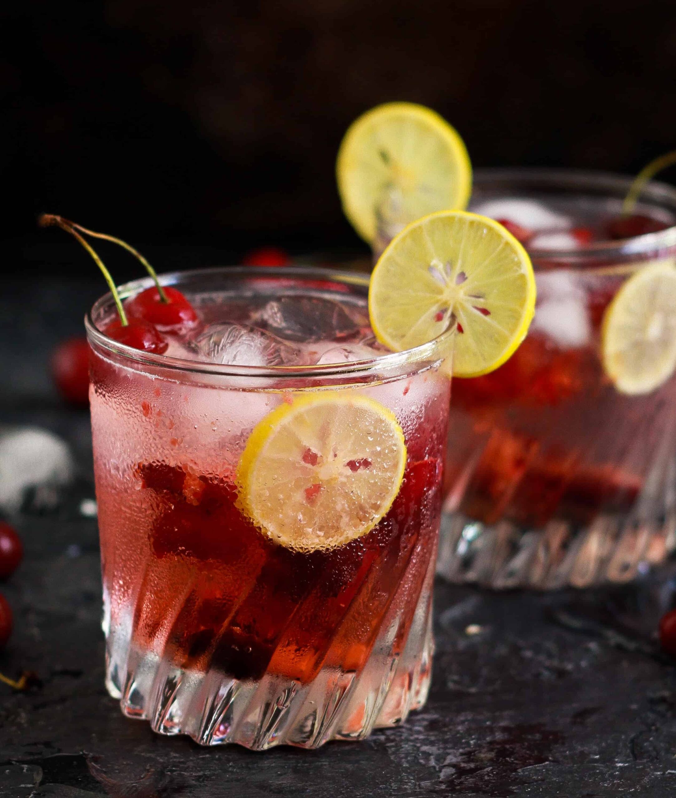 Cherry Gin And Tonic in a glass garnished with lemon slice.