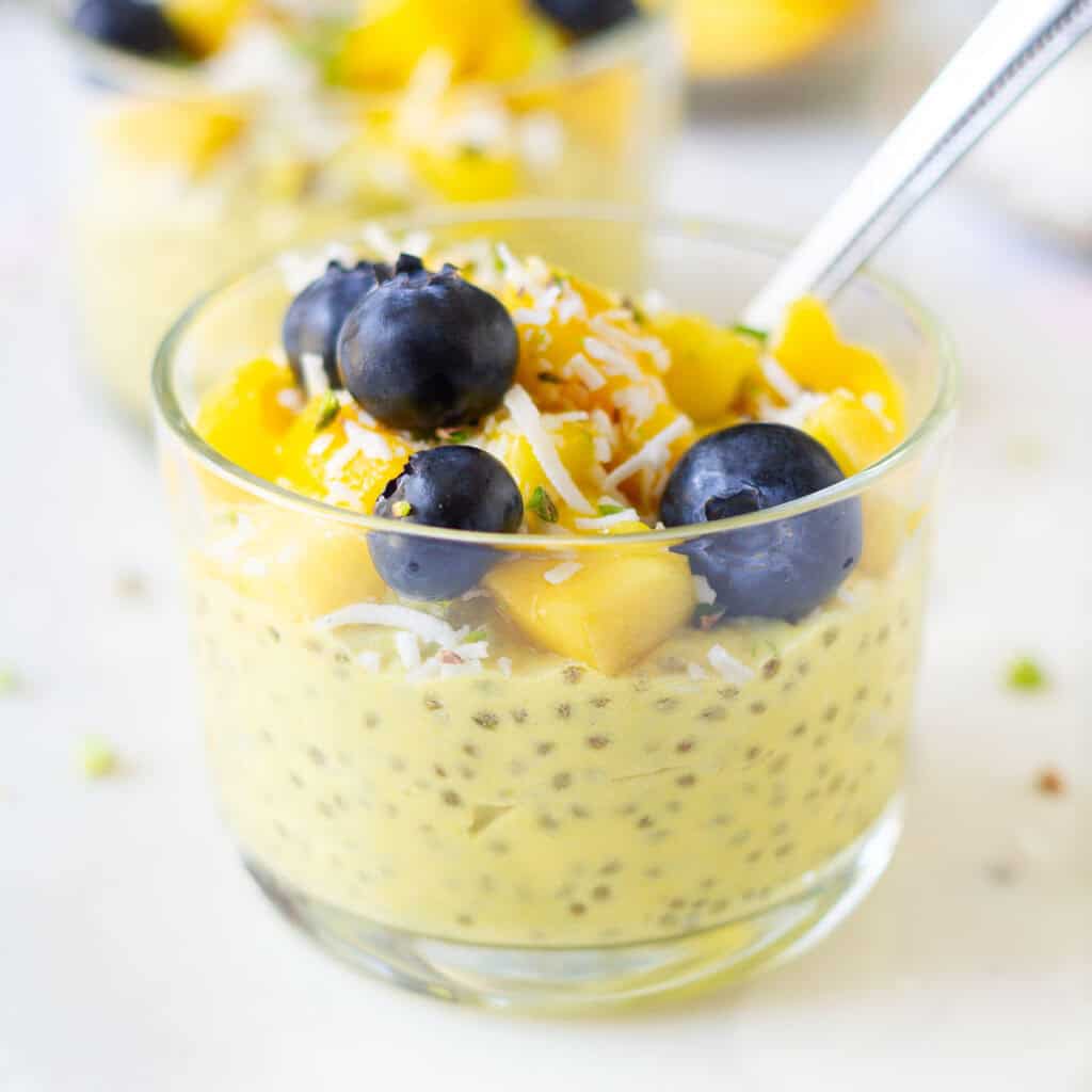 mango chia pudding topped with coconut, mangoes, and blueberries in a glass.