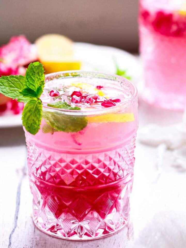 Pomegranate mojito in a glass garnished with mint and lime.