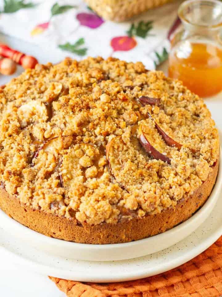 Apple crumb cake on a serving platter with ingredients in the background.