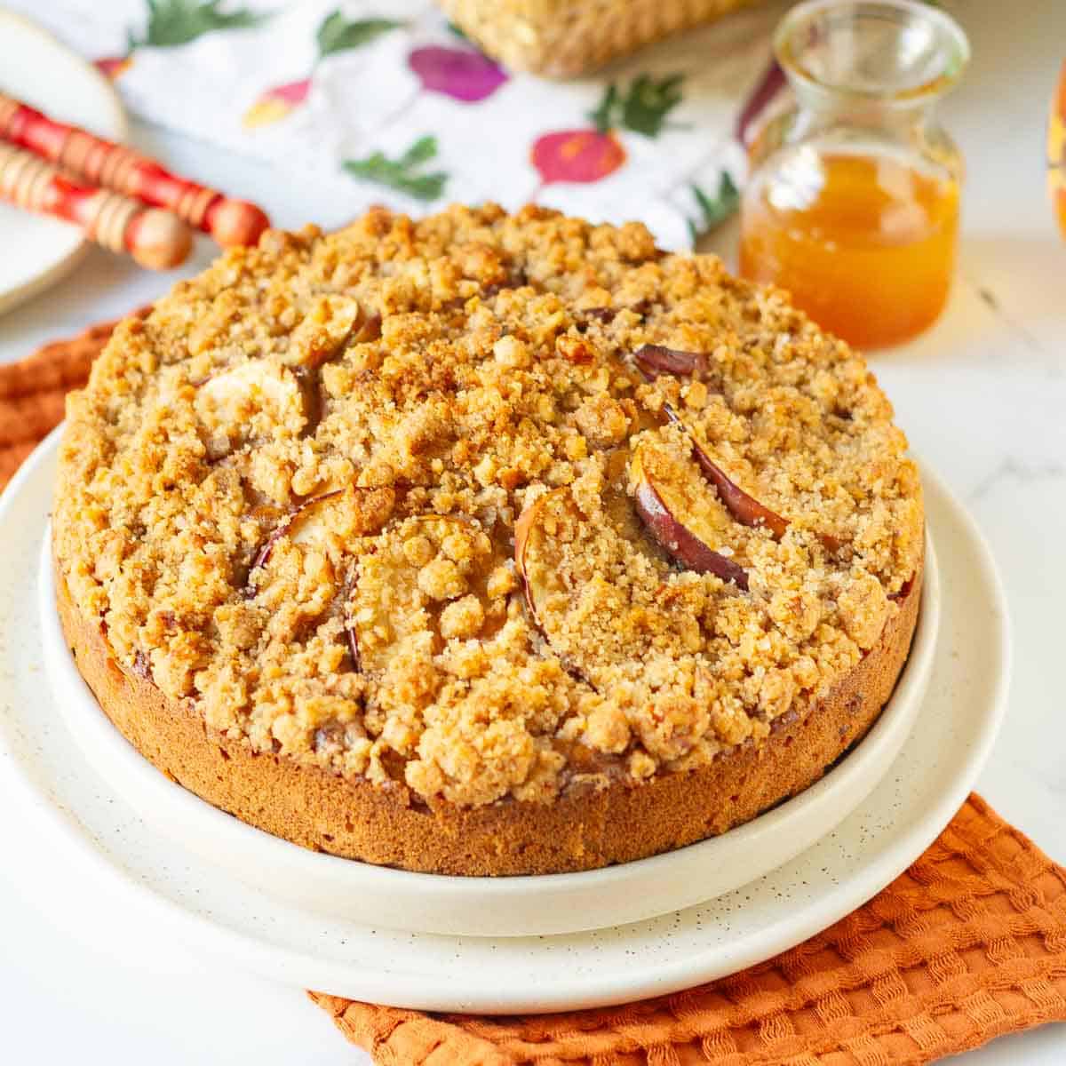 Apple crumb cake on a serving platter with ingredients in the background.