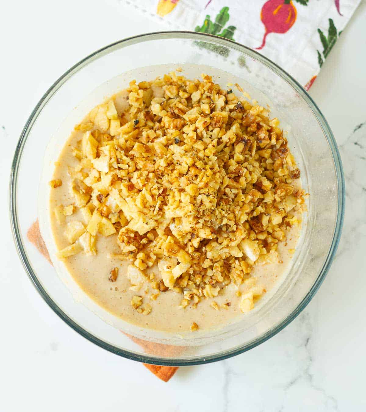 Chopped apples and walnuts on top of cake batter in a mixing bowl.